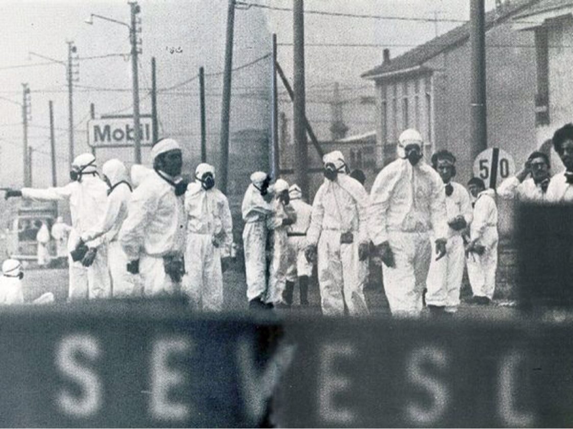 Equips amb vestits de protecció i màscares antigàs en un carrer de Seveso el 1976; en primer pla, el rètol amb el nom del poble
